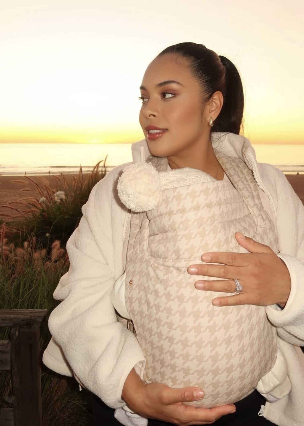 Woman wearing patterned baby carrier and cream sweater at sunset on the beach