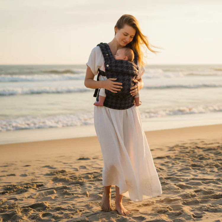 Mother using soft baby carrier on sandy beach at sunset