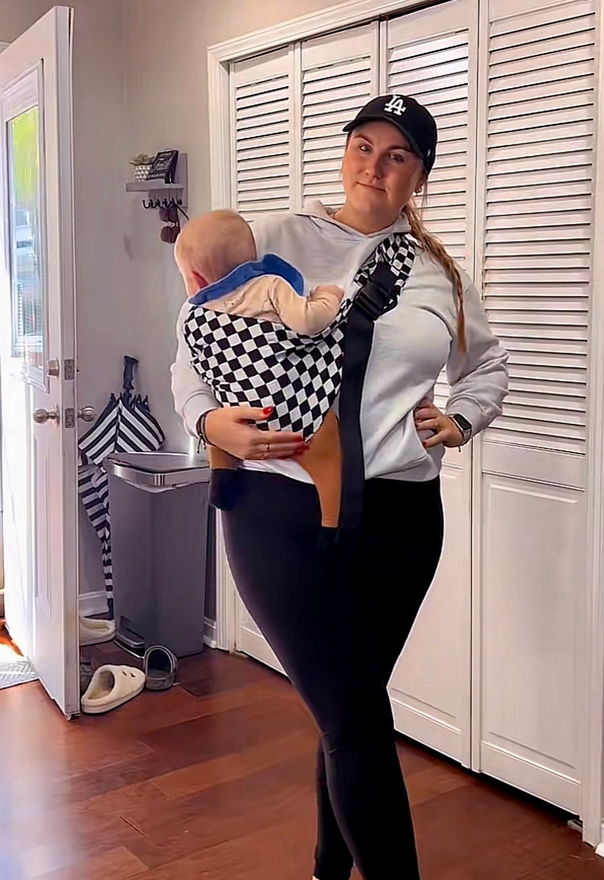 Woman carrying baby in checkered sling baby carrier indoors