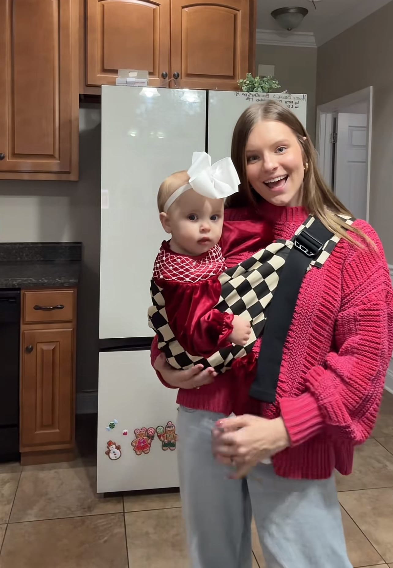 Mother smiling while wearing baby in checkered sling carrier in kitchen