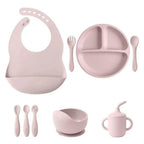 Pink silicone baby feeding set with bib, divided plate, utensils, suction bowl, and sippy cup.