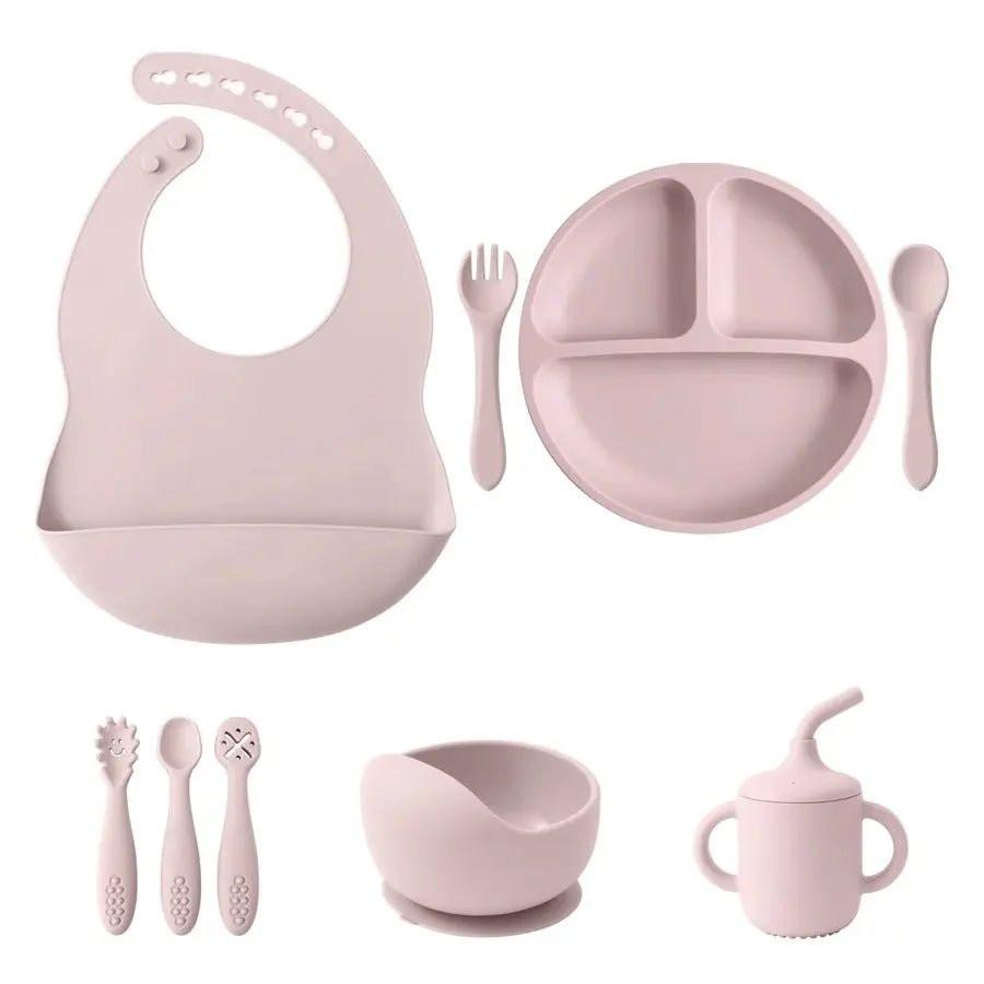 Pink silicone baby feeding set with bib, divided plate, utensils, suction bowl, and sippy cup.