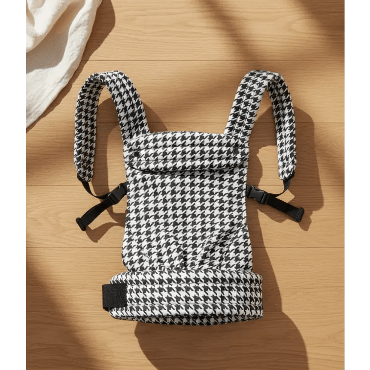 Houndstooth patterned baby carrier with padded straps on wood floor