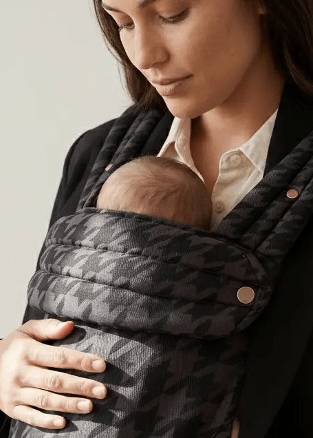 Parent carrying infant in patterned gray baby carrier