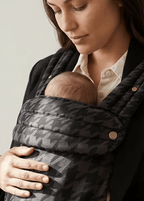 Parent carrying infant in patterned gray baby carrier